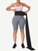 Woman wrapping a long black latex tummy wrap band around her waist, front view.