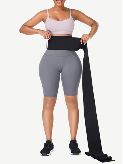Woman wrapping a long black latex tummy wrap band around her waist, front view.