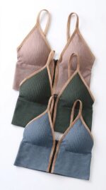 Three ribbed front-zip wire-free bralettes in dusty rose, forest green and slate blue with tan contrast binding, laid flat together.