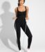 Woman in black zip-front sauna jumpsuit holding a resistance band, front view.