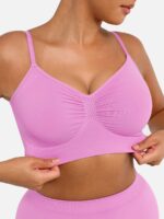 Woman wearing the candy pink seamless shaping bra with adjustable straps, holding the strap.