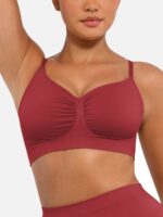 Woman wearing the dark red seamless shaping bra with adjustable straps, holding the strap.