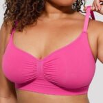 Woman wearing the hot pink seamless shaping bra with adjustable straps, holding the strap.