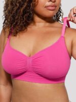 Woman wearing the hot pink seamless shaping bra with adjustable straps, holding the strap.