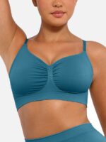 Woman wearing the teal blue seamless shaping bra with adjustable straps, holding the strap.