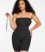 Woman in black strapless butt-lifting bodysuit holding a detachable strap, front view.